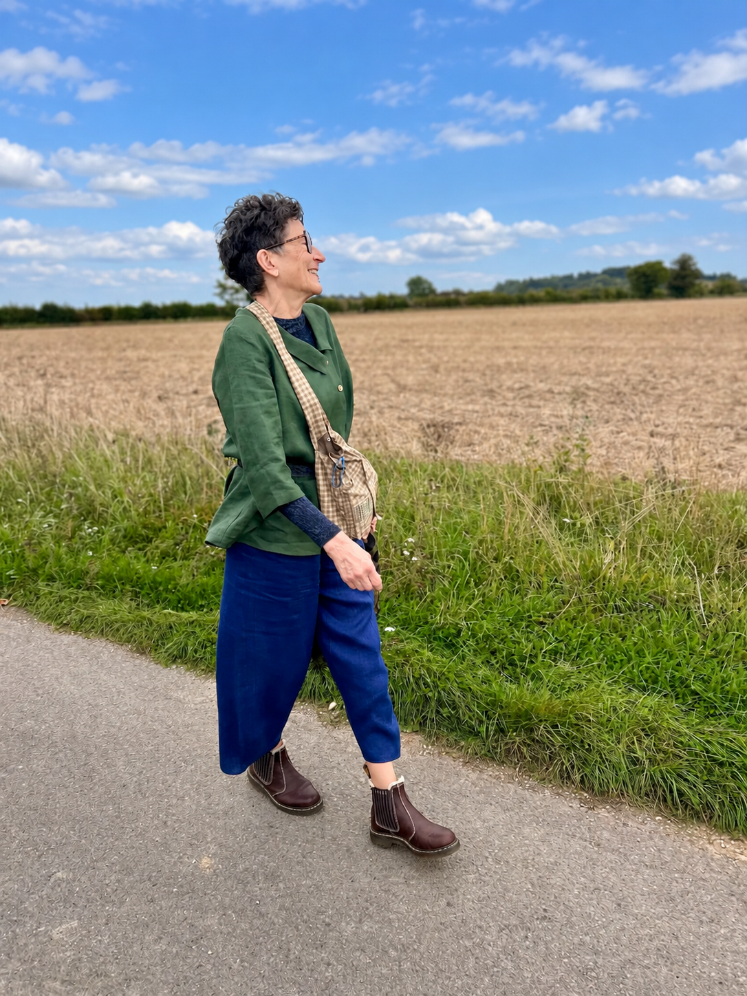 Isobel walking in her olive green tunic, blue linen trousers and brown boots